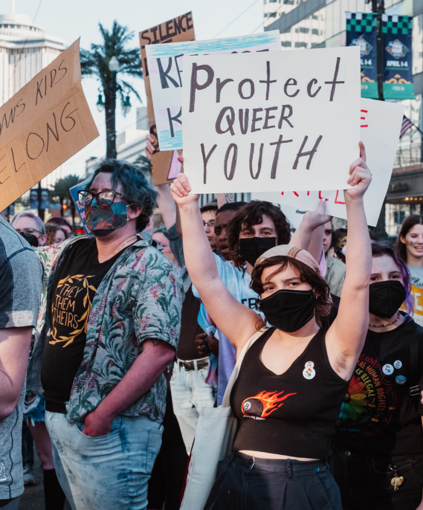 Person holding up a sign that says Protect Queer Youth amid a crowd of other protestors.